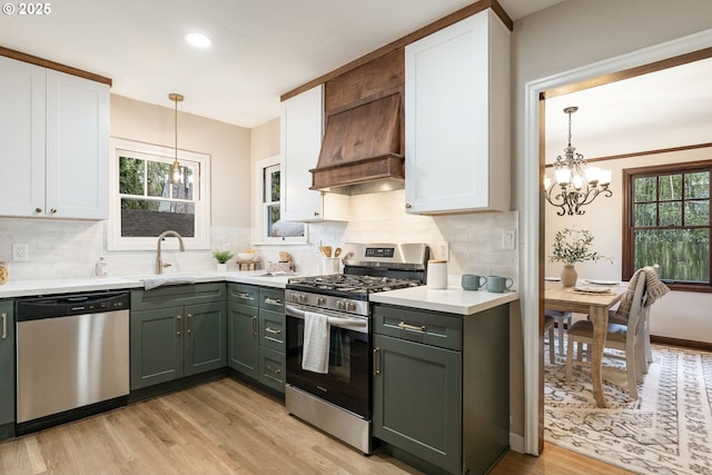 5932 NE 29th Ave, Portland, OR 97211 - kitchen with stainless steel appliances, custom range hood, a sink, a chandelier, and white cabinetry