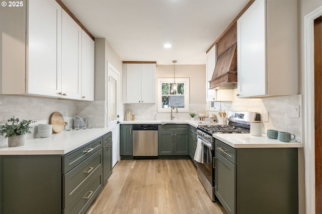 5932 NE 29th Ave, Portland, OR 97211 - kitchen with stainless steel appliances, a sink, custom exhaust hood, white cabinetry, and light wood-type flooring