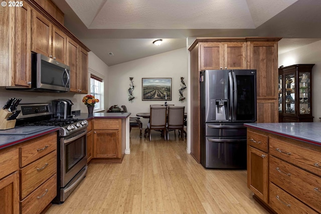 6783 Rogue River Dr, Shady Cove, OR 97539 - kitchen featuring appliances with stainless steel finishes, dark countertops, light wood finished floors, lofted ceiling, and brown cabinets