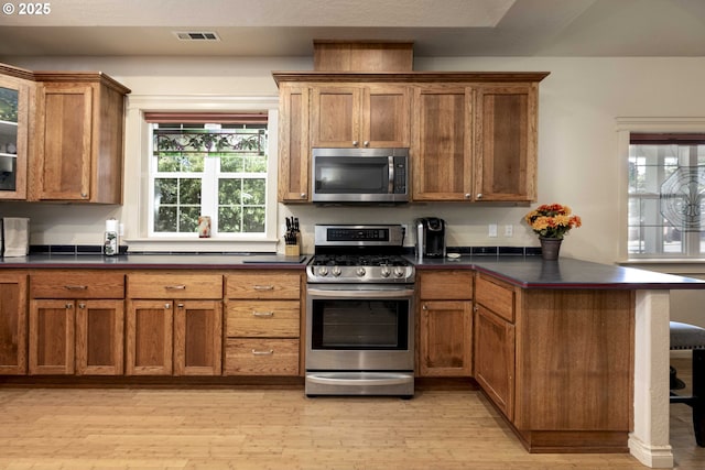 6783 Rogue River Dr, Shady Cove, OR 97539 - kitchen with stainless steel appliances, brown cabinetry, light wood-style flooring, a peninsula, and dark countertops