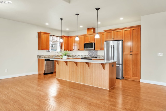 kitchen featuring pendant lighting, a breakfast bar, stainless steel appliances, a center island, and light wood-type flooring