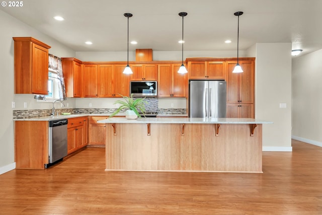 kitchen with a kitchen bar, a center island, hanging light fixtures, light hardwood / wood-style flooring, and stainless steel appliances