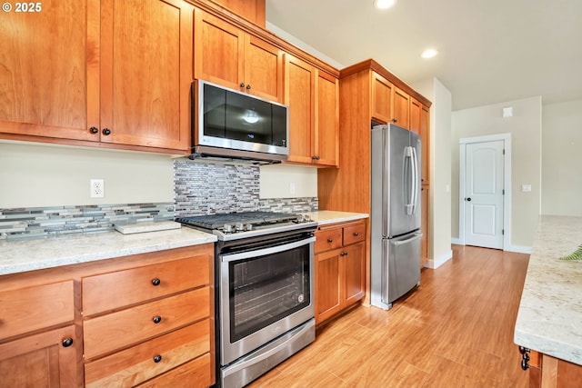 kitchen with stainless steel appliances, light stone countertops, decorative backsplash, and light hardwood / wood-style flooring