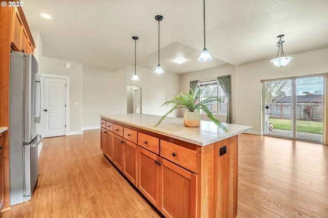 kitchen with light hardwood / wood-style flooring, stainless steel refrigerator, hanging light fixtures, a center island, and light stone countertops