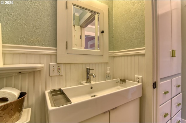5120 NE Glisan St, Portland, OR 97213 - bathroom with a textured wall, a wainscoted wall, a sink, and a decorative wall