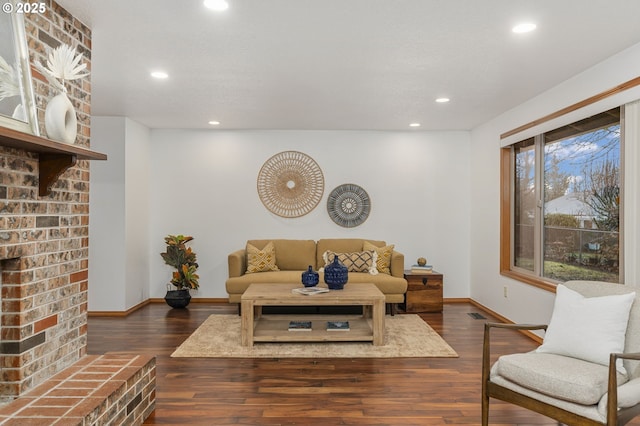 living area featuring baseboards, dark wood-style flooring, a brick fireplace, and recessed lighting