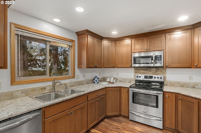 kitchen featuring stainless steel appliances, light wood-style flooring, brown cabinetry, a sink, and light stone countertops