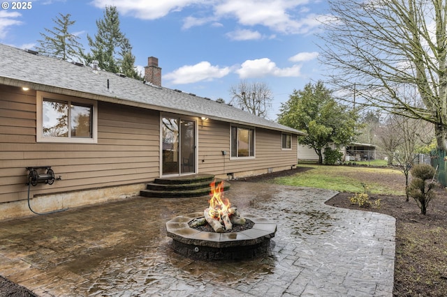 back of house with entry steps, an outdoor fire pit, a chimney, roof with shingles, and a patio area