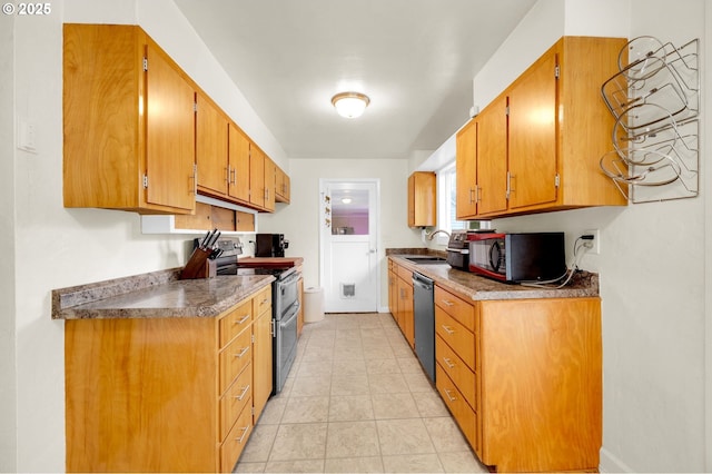 kitchen with appliances with stainless steel finishes, brown cabinetry, a sink, and light tile patterned flooring