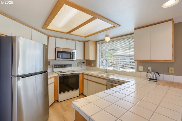 kitchen featuring tile countertops, white cabinetry, sink, stainless steel appliances, and light wood-type flooring