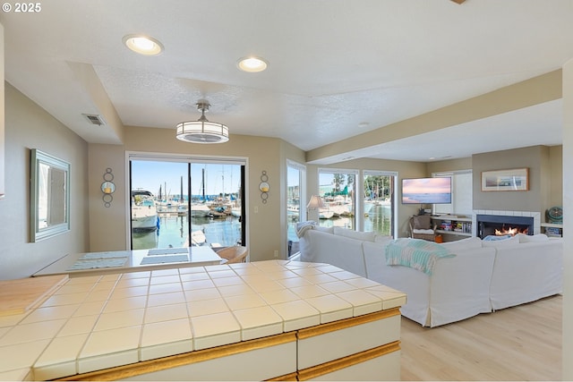 kitchen with light hardwood / wood-style flooring, a fireplace, tile counters, and a textured ceiling