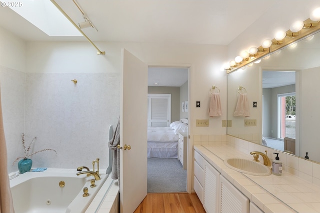 bathroom featuring a relaxing tiled tub, vanity, a skylight, and hardwood / wood-style flooring