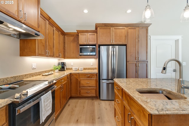 4080 Caddington Ln, Florence, OR 97439 - kitchen with appliances with stainless steel finishes, under cabinet range hood, brown cabinets, light wood finished floors, and decorative light fixtures