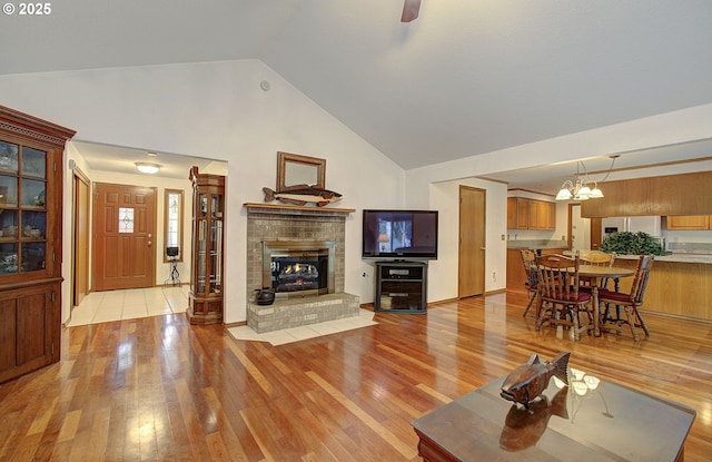 living room with high vaulted ceiling, a fireplace, an inviting chandelier, and light wood-style floors