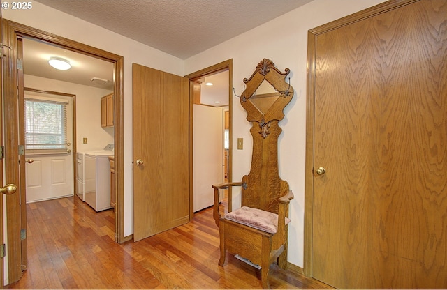 hallway featuring a textured ceiling, light wood finished floors, and independent washer and dryer