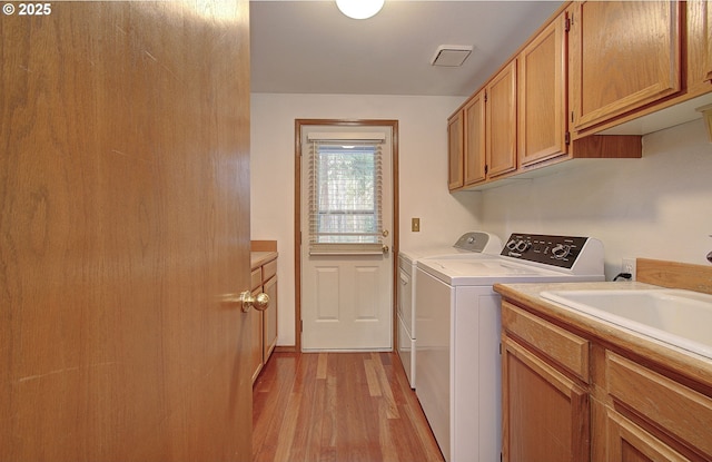 laundry room featuring visible vents, cabinet space, light wood-style flooring, a sink, and separate washer and dryer