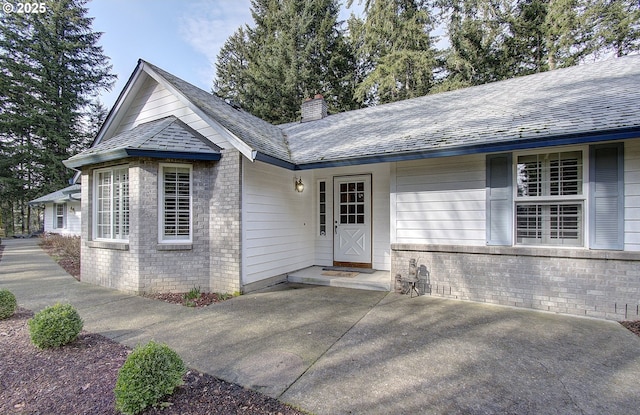 property entrance with brick siding, a chimney, and roof with shingles