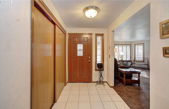 foyer featuring light carpet, light tile patterned floors, baseboards, and a textured ceiling