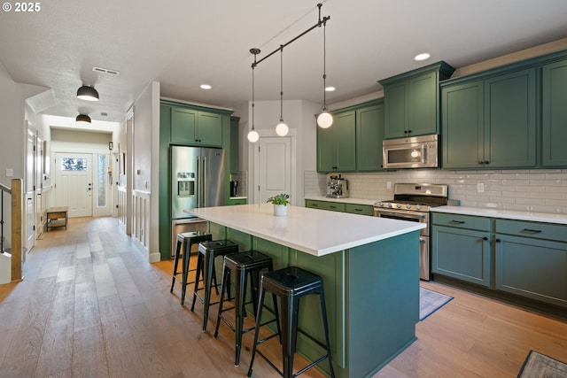 12721 Cottonwood Ave, Oregon City, OR 97045 - kitchen with stainless steel appliances, green cabinets, a center island, a breakfast bar area, and decorative backsplash