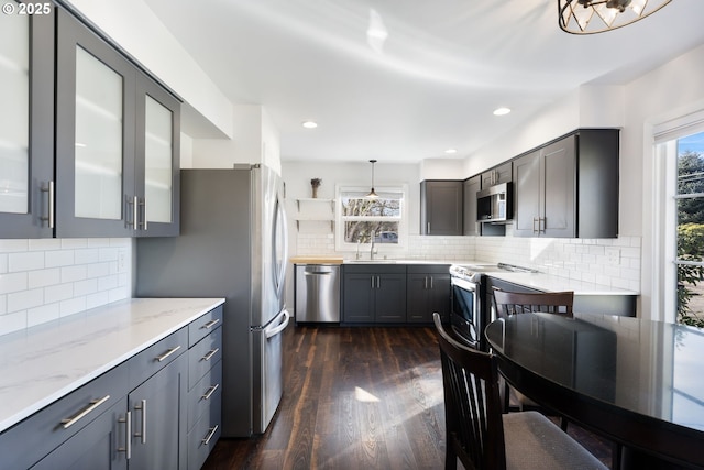 kitchen with glass insert cabinets, appliances with stainless steel finishes, dark wood-style flooring, light stone countertops, and a sink