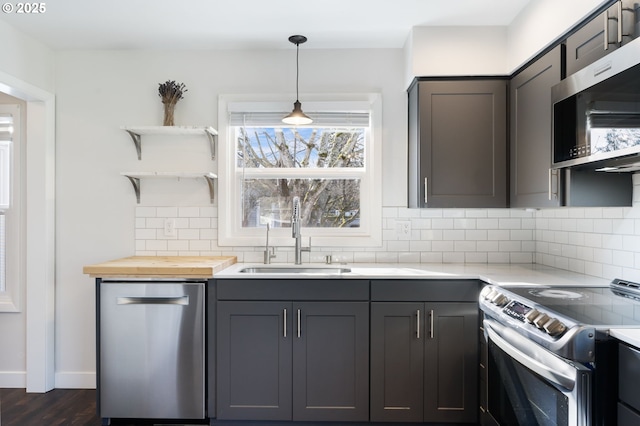 kitchen featuring a sink, appliances with stainless steel finishes, backsplash, open shelves, and decorative light fixtures