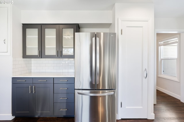 kitchen with light countertops, freestanding refrigerator, dark wood-style floors, tasteful backsplash, and glass insert cabinets