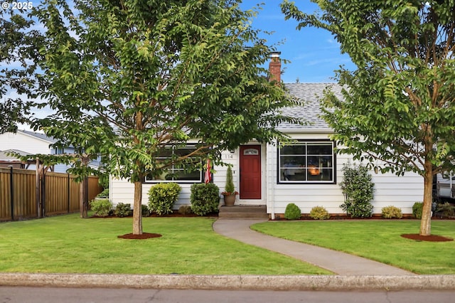 obstructed view of property with a shingled roof, a chimney, a front yard, and fence