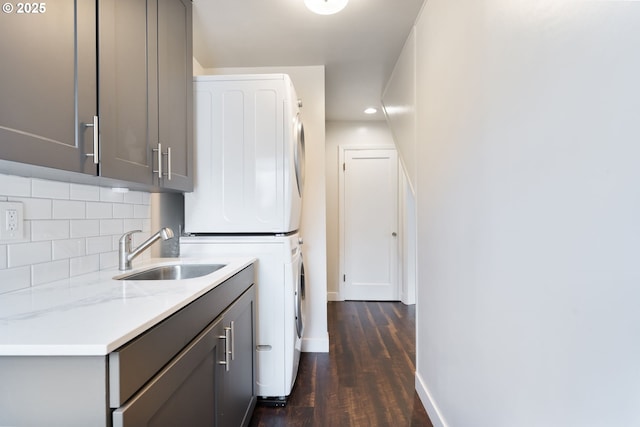 laundry area with cabinet space, baseboards, dark wood finished floors, stacked washer / dryer, and a sink