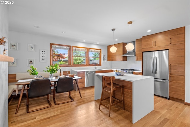 3905 NE Holman St, Portland, OR 97211 - kitchen featuring appliances with stainless steel finishes, wall chimney exhaust hood, light countertops, a kitchen island, and brown cabinetry