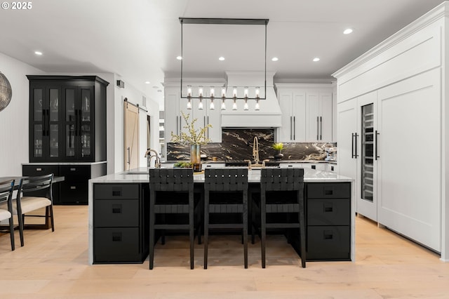 kitchen with decorative backsplash, a barn door, a center island with sink, white cabinets, and hanging light fixtures