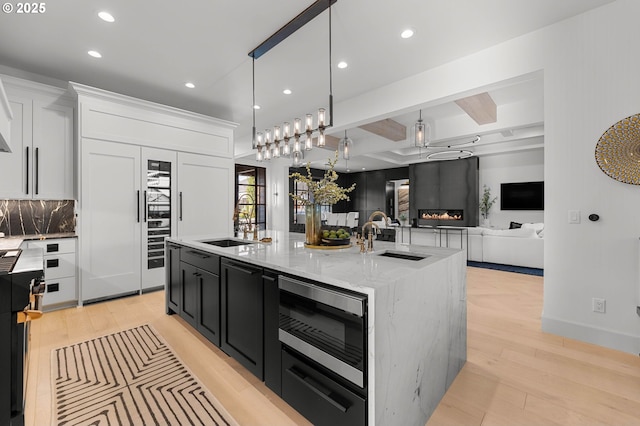 kitchen featuring white cabinets, an island with sink, stainless steel microwave, and sink