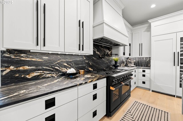 kitchen with decorative backsplash, custom exhaust hood, double oven range, dark stone countertops, and white cabinets