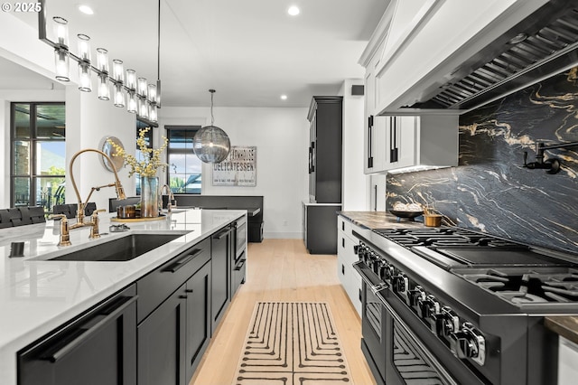 kitchen with light stone countertops, dishwasher, white cabinetry, sink, and premium range hood