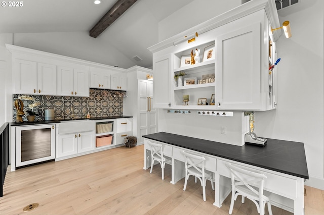 kitchen with light wood-type flooring, tasteful backsplash, white cabinets, vaulted ceiling with beams, and wine cooler