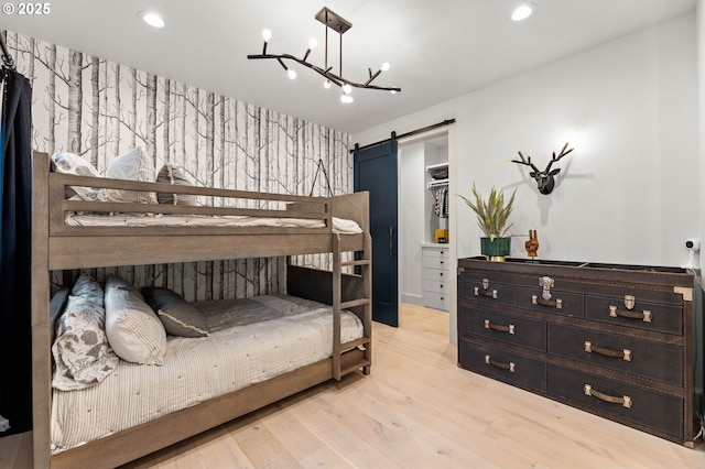 bedroom with a chandelier, a barn door, a closet, and light hardwood / wood-style flooring