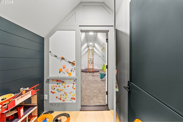 recreation room featuring wood walls, light hardwood / wood-style flooring, and vaulted ceiling