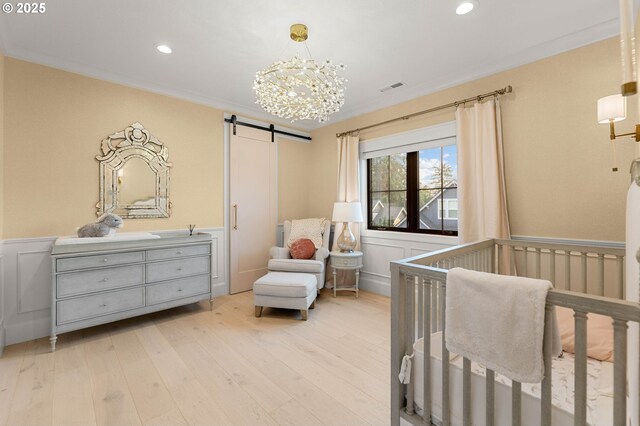 bedroom featuring a barn door, light hardwood / wood-style flooring, a nursery area, and ornamental molding