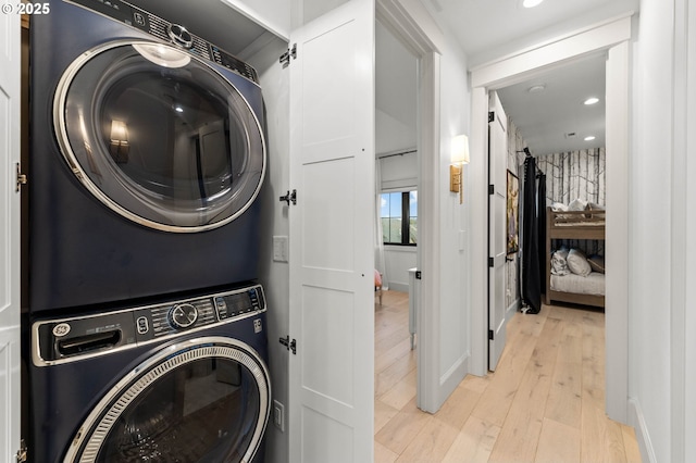 laundry area with light hardwood / wood-style flooring and stacked washer / drying machine