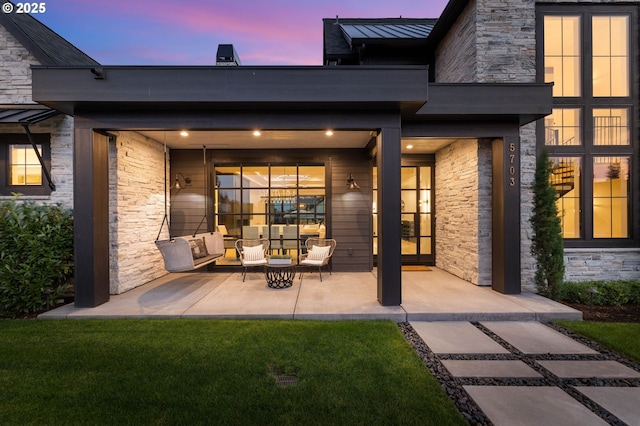 exterior entry at dusk featuring a patio, outdoor lounge area, a standing seam roof, metal roof, and stone siding