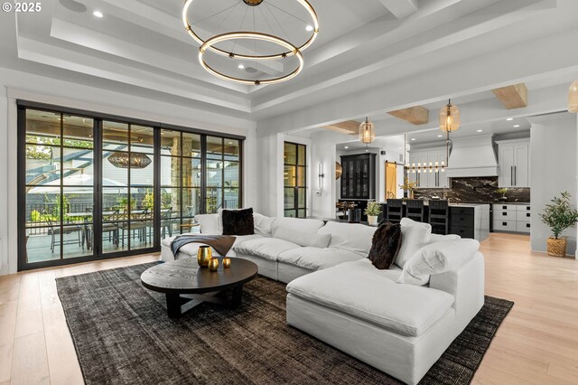 living room with a towering ceiling, a tray ceiling, light hardwood / wood-style flooring, and a notable chandelier