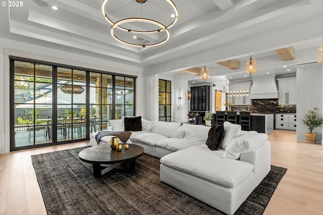 living room featuring a chandelier, light wood finished floors, and a raised ceiling