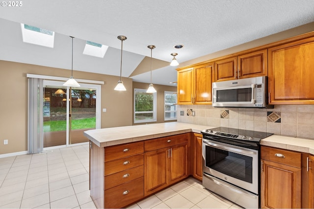 kitchen featuring vaulted ceiling with skylight, appliances with stainless steel finishes, brown cabinetry, and a peninsula
