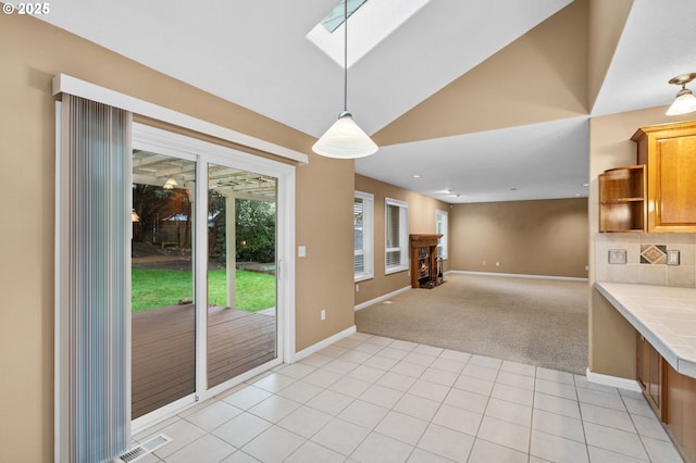 unfurnished dining area featuring a warm lit fireplace, light carpet, baseboards, a skylight, and visible vents