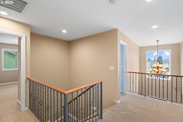 corridor featuring visible vents, carpet floors, a chandelier, and an upstairs landing