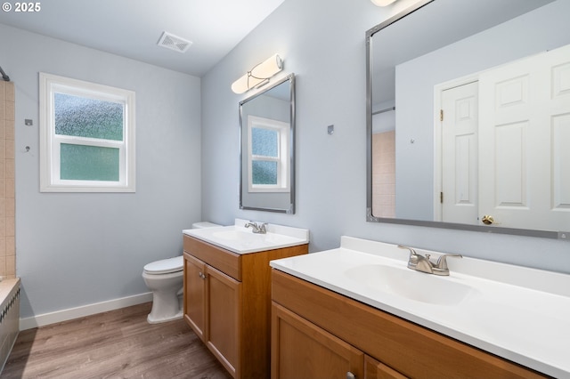 full bath with visible vents, wood finished floors, toilet, two vanities, and a sink