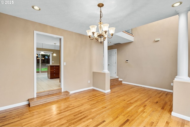 unfurnished dining area featuring an inviting chandelier, light wood-style floors, baseboards, recessed lighting, and ornate columns