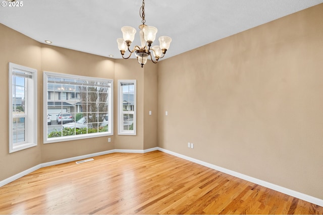 spare room with baseboards, light wood-style flooring, a notable chandelier, and visible vents