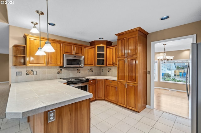 kitchen featuring open shelves, a peninsula, brown cabinets, appliances with stainless steel finishes, and a notable chandelier