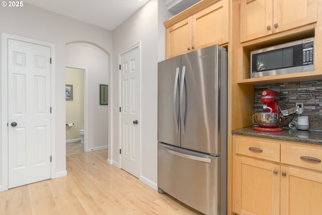 kitchen featuring decorative backsplash, light hardwood / wood-style flooring, appliances with stainless steel finishes, light brown cabinets, and dark stone counters