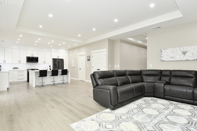 living area with visible vents, light wood finished floors, baseboards, a tray ceiling, and recessed lighting